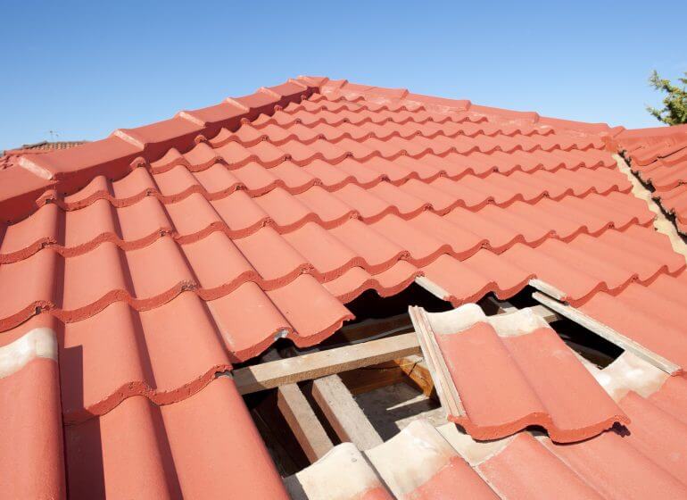 A red tiled roof with a hole in it that requires preparations for roof replacement.