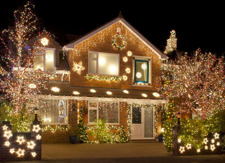 A house is adorned with festive holiday lights, carefully avoiding potential damages to the roof.