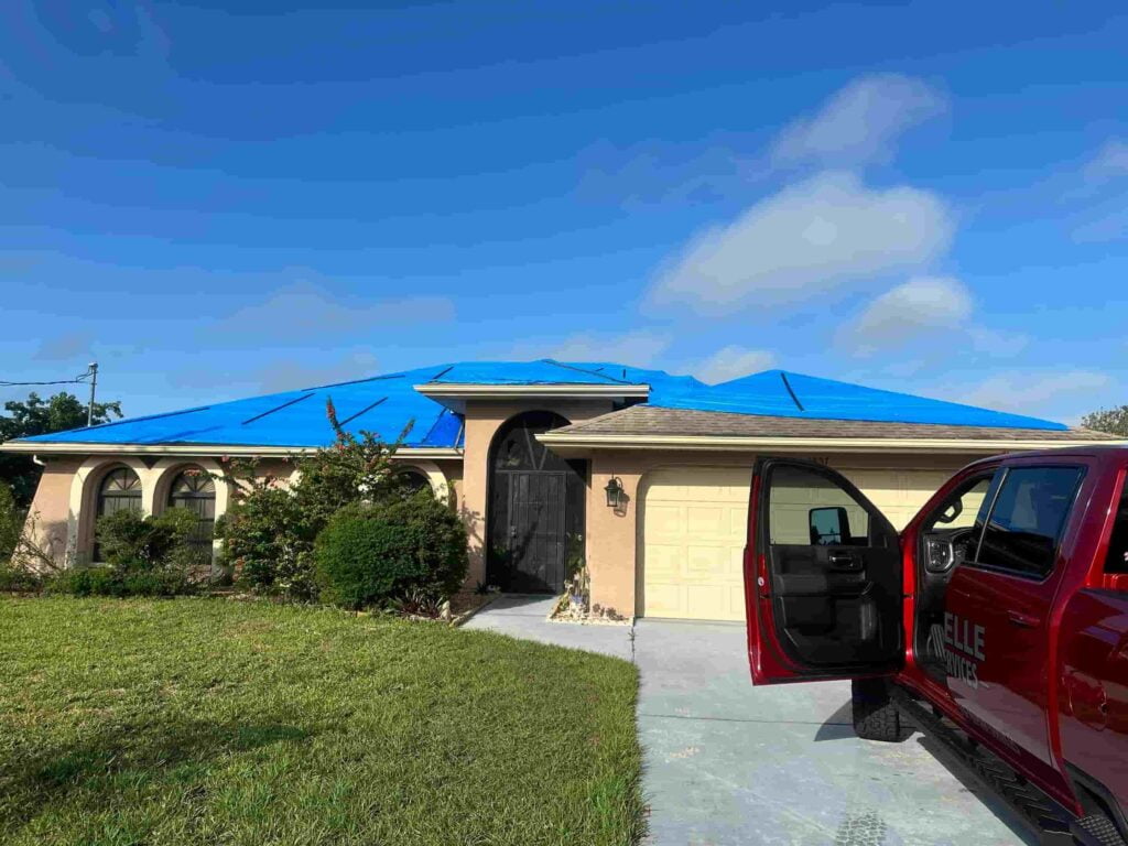 A truck is parked in front of a house with a blue tarp used for emergency roof tarping.